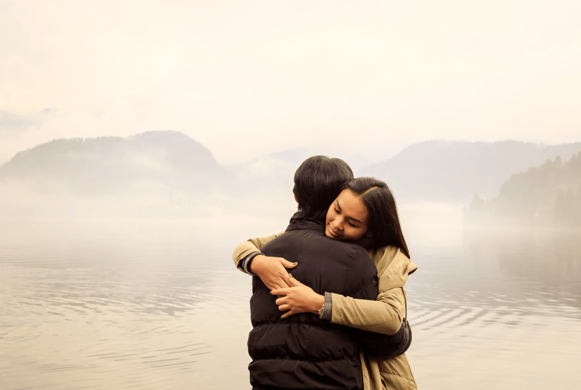 Romantic couple hugging by misty lake in autumn