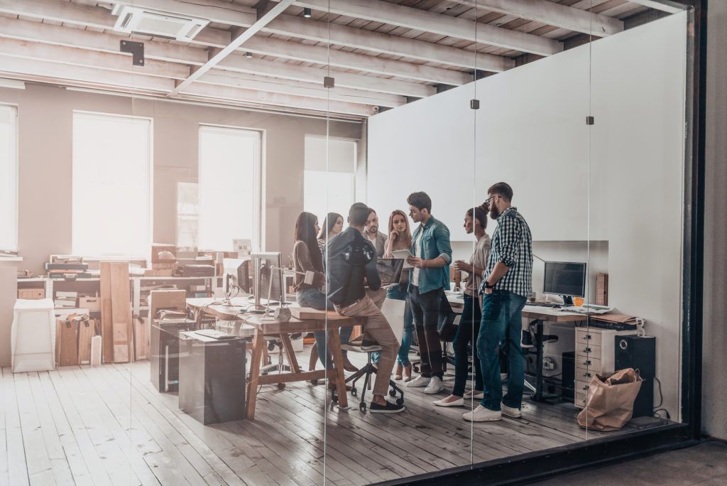 Teamwork in action. Full length of young modern people in smart casual wear discussing business while standing behind the glass wall in the creative office